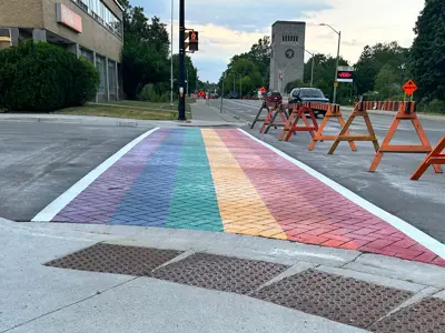 Rainbow sidewalk freshly installed with traffic barrier in front and the Carillon tower is seen in the background.